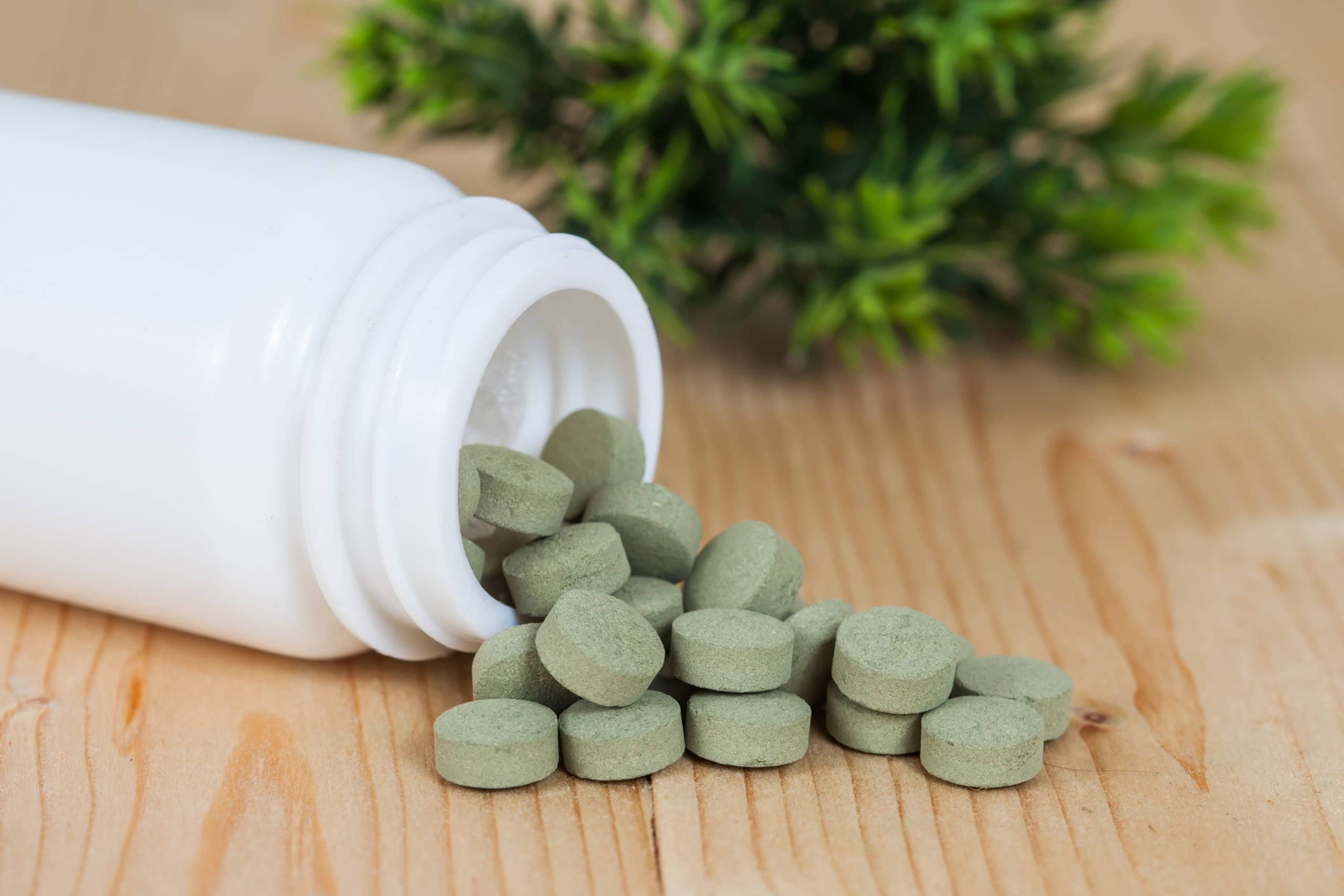 Grüne Tabletten fallen aus einer weißen Pillenpackung auf Holz.